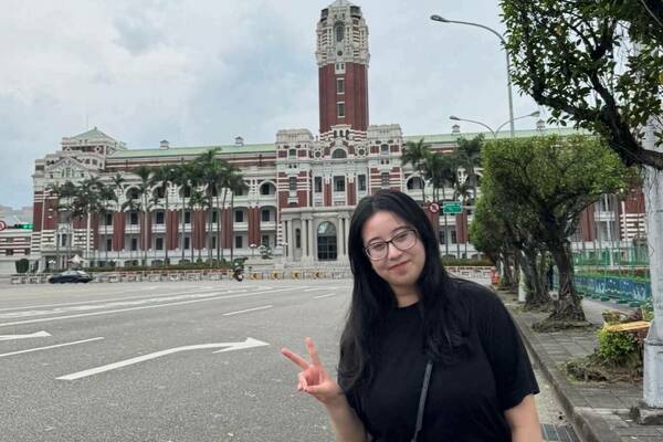 A person wearing a black shirt and glasses makes a peace sign in front of the Presidential Office Building in Taipei, Taiwan.