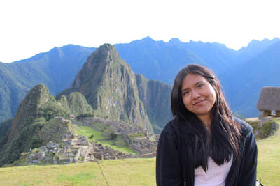 Young woman in black jacket smiling in front of Machu Picchu's green terraced ruins and towering mountains.