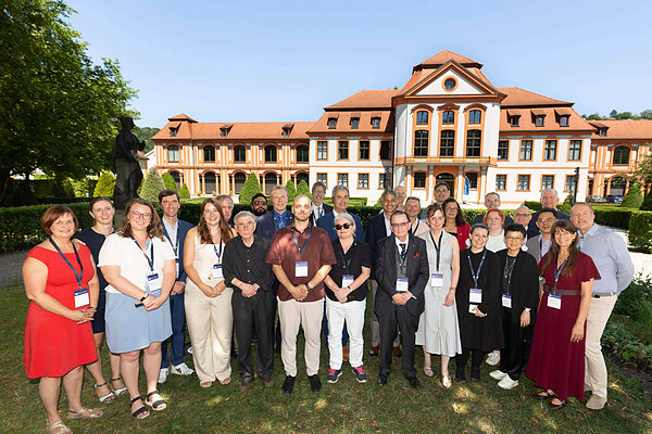Group of attendees posing in front of a grand building with orange tiled roofs.